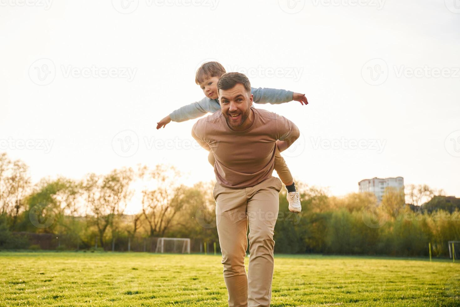 Wellbeing, kid ,is, on, the shoulders or back. Happy father with son are having fun on the field at summertime photo