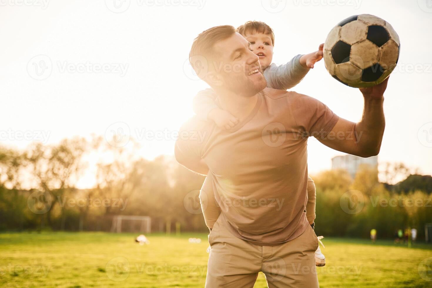 On ,shoulders, with, soccer ball. Happy father with son are having fun on the field at summertime photo
