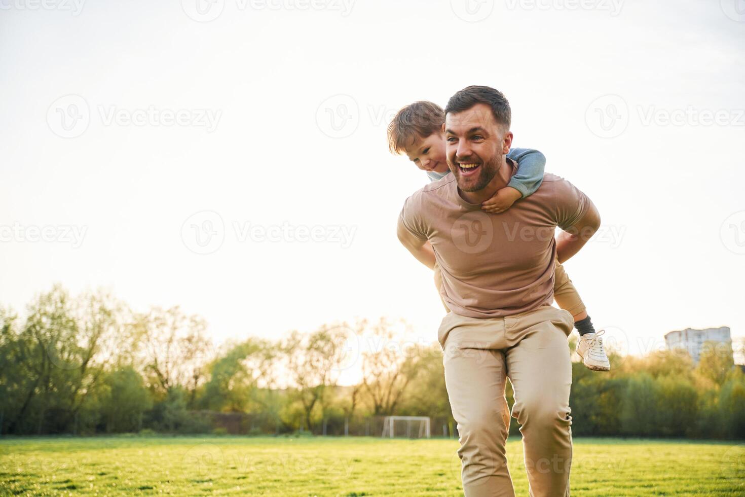 Wellbeing, kid is ,on, the ,shoulders or back. Happy father with son are having fun on the field at summertime photo