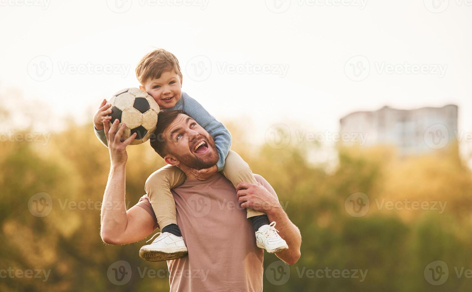 On, shoulders,,, with soccer ball. Happy father with son are having fun on the field at summertime photo