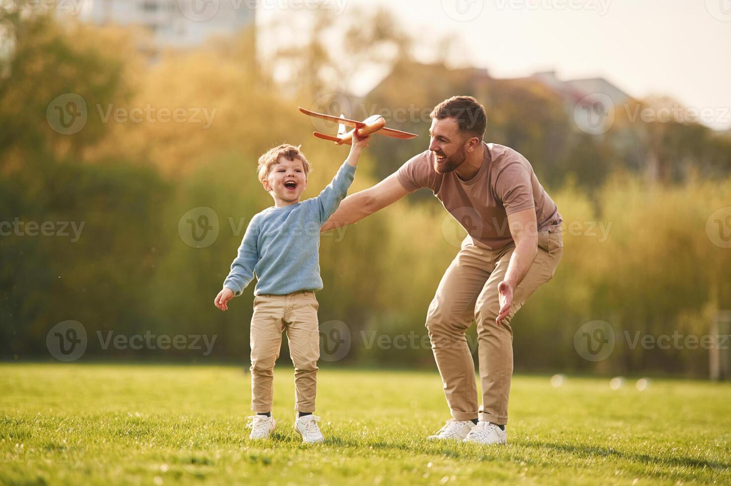 In casual ,,clothes. Running with toy ,plane. Happy father with son are having fun on the field at summertime photo