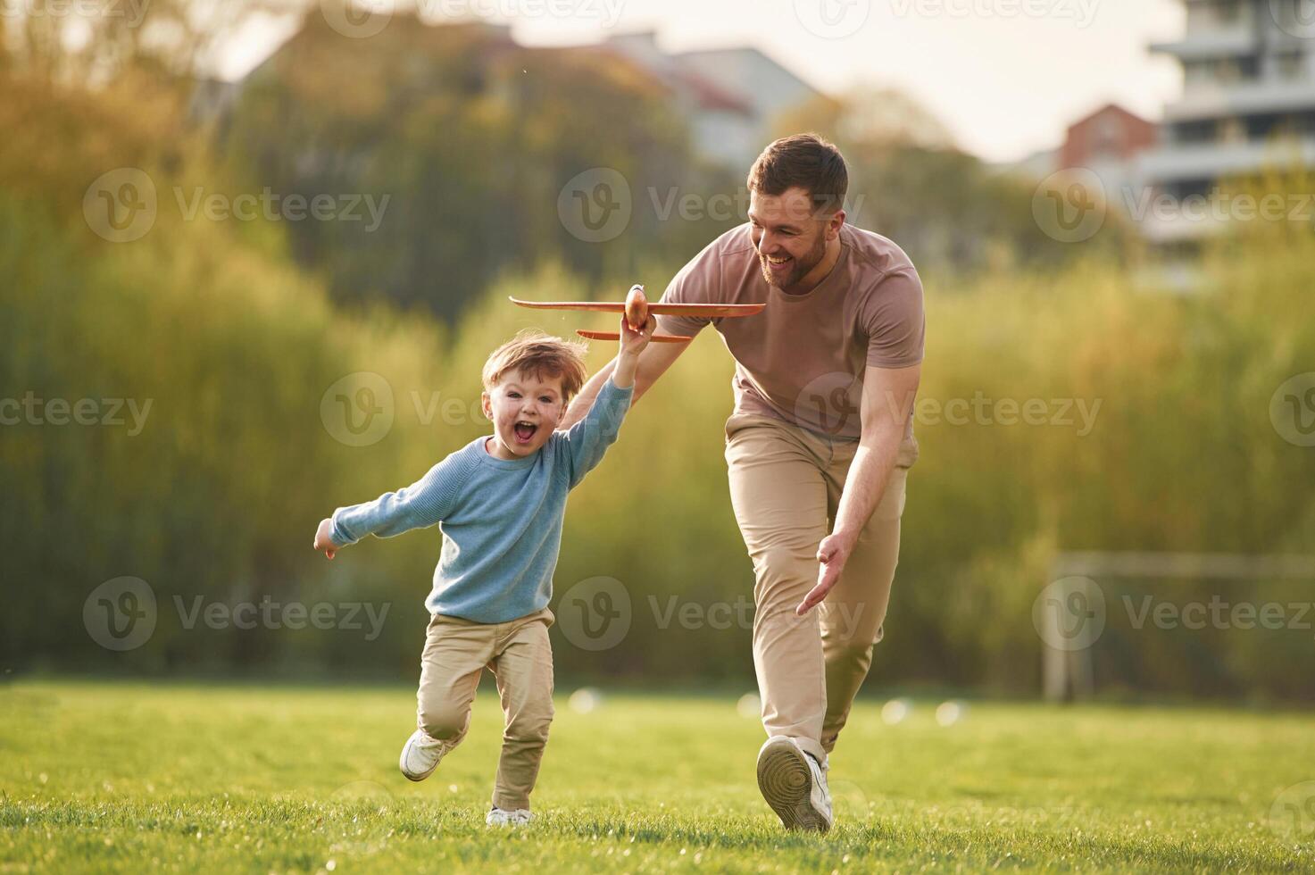 Flying high, holding toy plane, running.,, Happy father with son are having fun on the field at summertime photo
