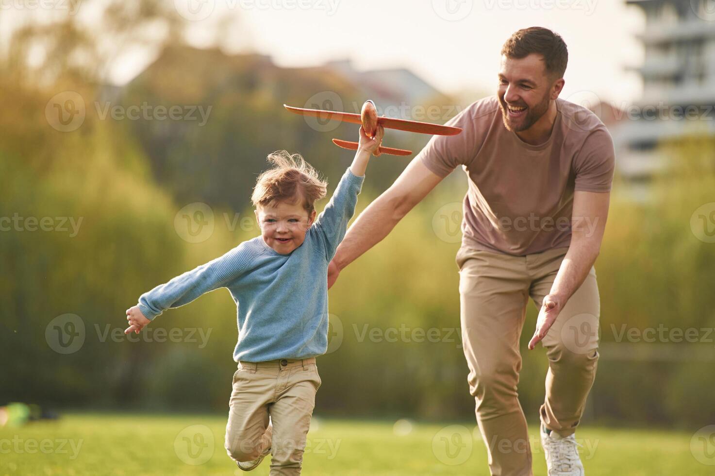 Flying high, holding toy,, plane, running. Happy father with son are having fun on the field at summertime photo