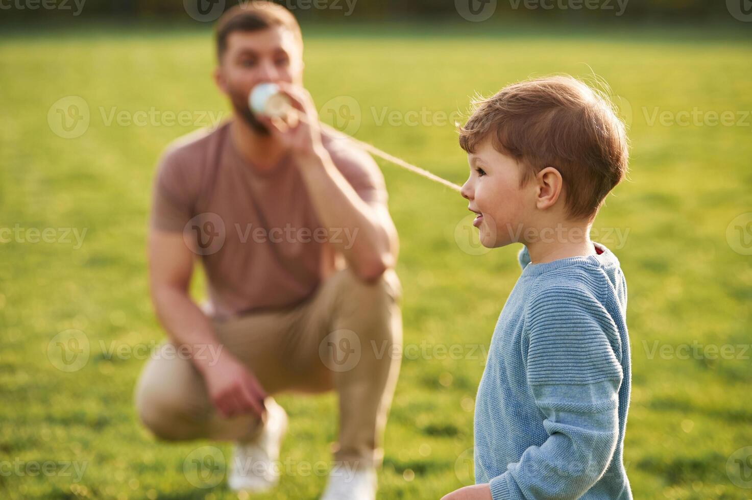 White paper cup telephone. Happy ,father, with son are having fun on the field at summertime photo