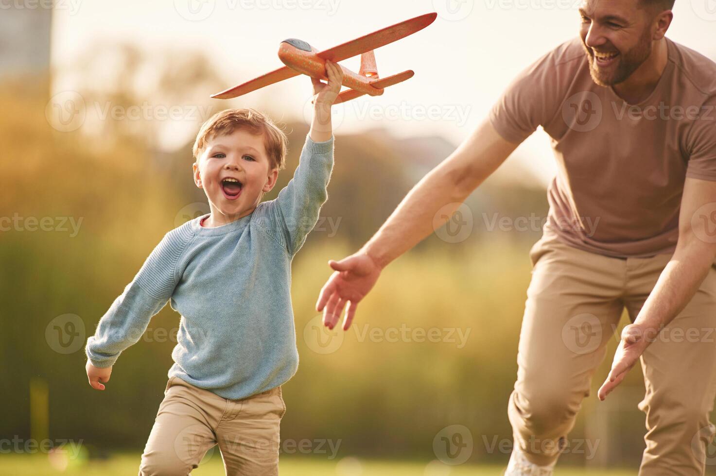 Flying, high, ,,holding toy plane, running. Happy father with son are having fun on the field at summertime photo
