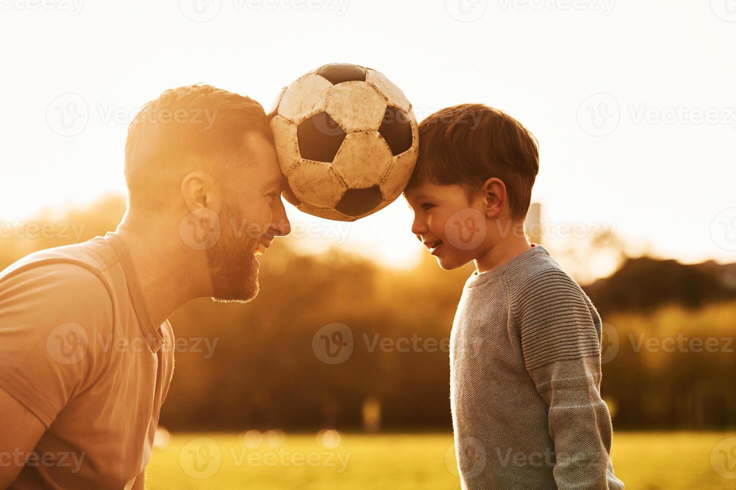 Positive emotions, holding soccer, ball ,by heads. Happy father with son are having fun on the field at summertime photo