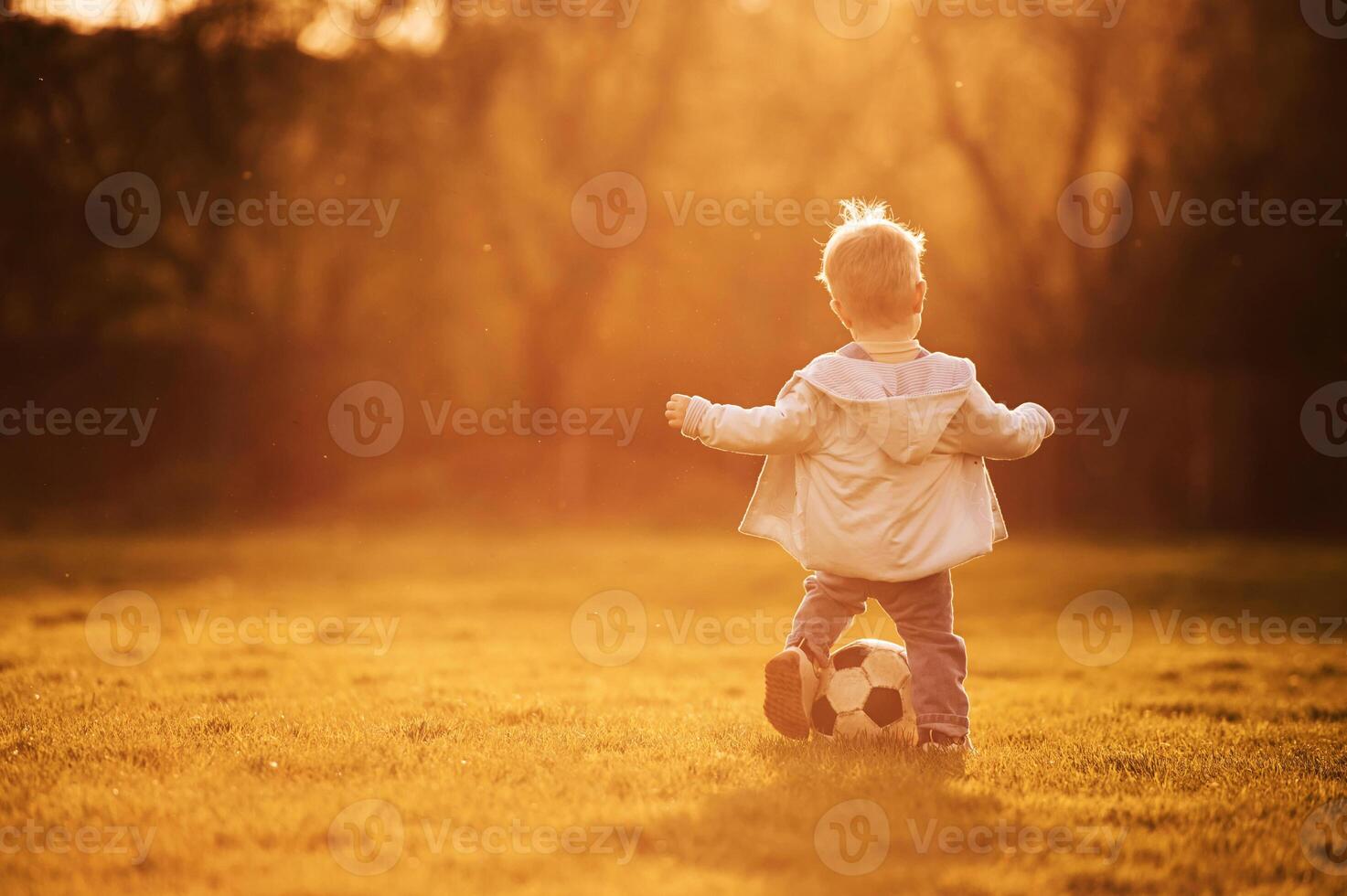 Playing with, soccer ball. Cute happy little boy is on the field outdoors photo