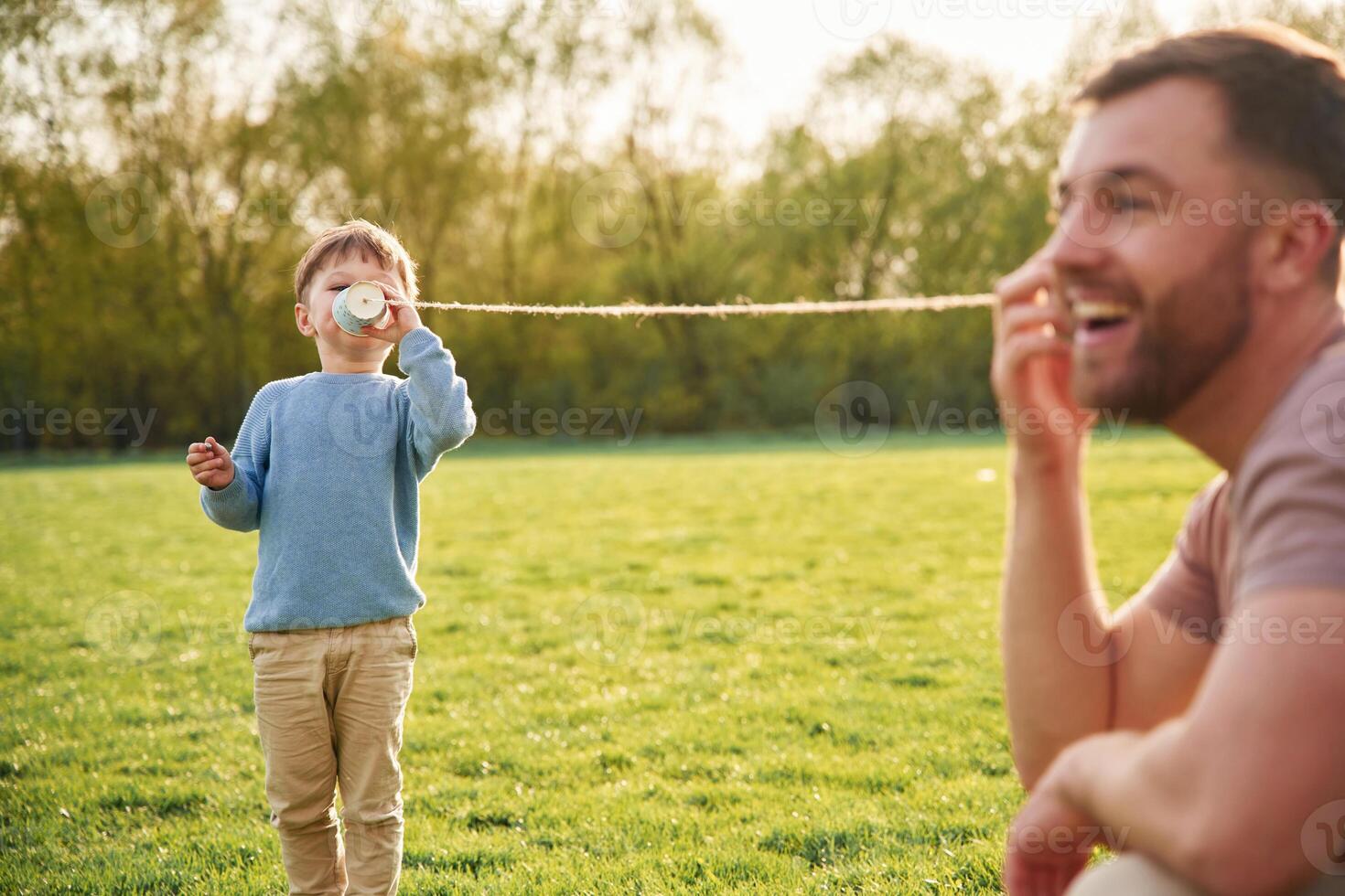 Talking by using paper ,cup telephone. Happy father with son are having fun on the field at summertime photo