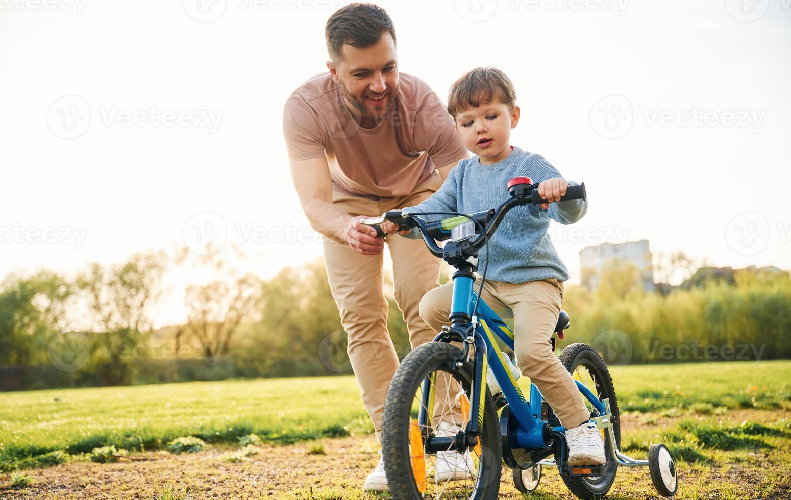 Trying the bicycle.. Happy father with son are having fun on the field at summertime photo