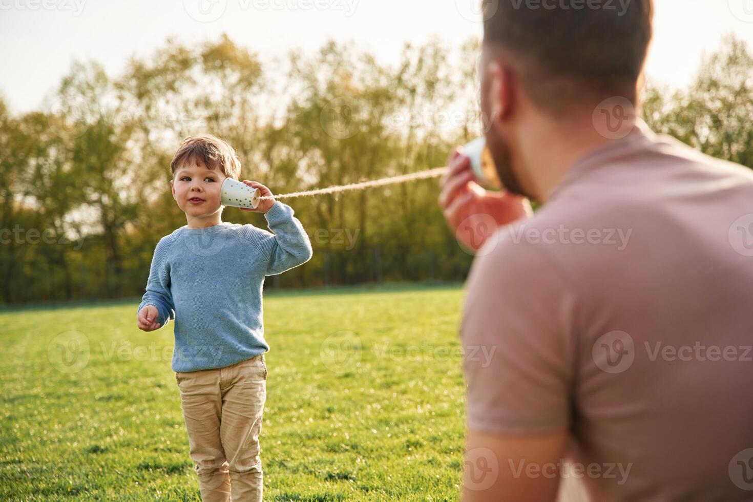 Using paper, cup telephone. Happy father with son are having fun on the field at summertime photo