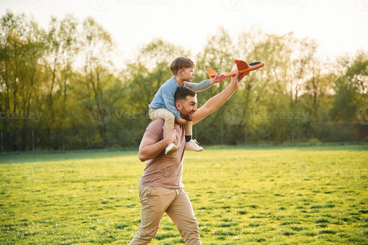 Orange ,colored ,toy plane, playing. Happy father with son are having fun on the field at summertime photo