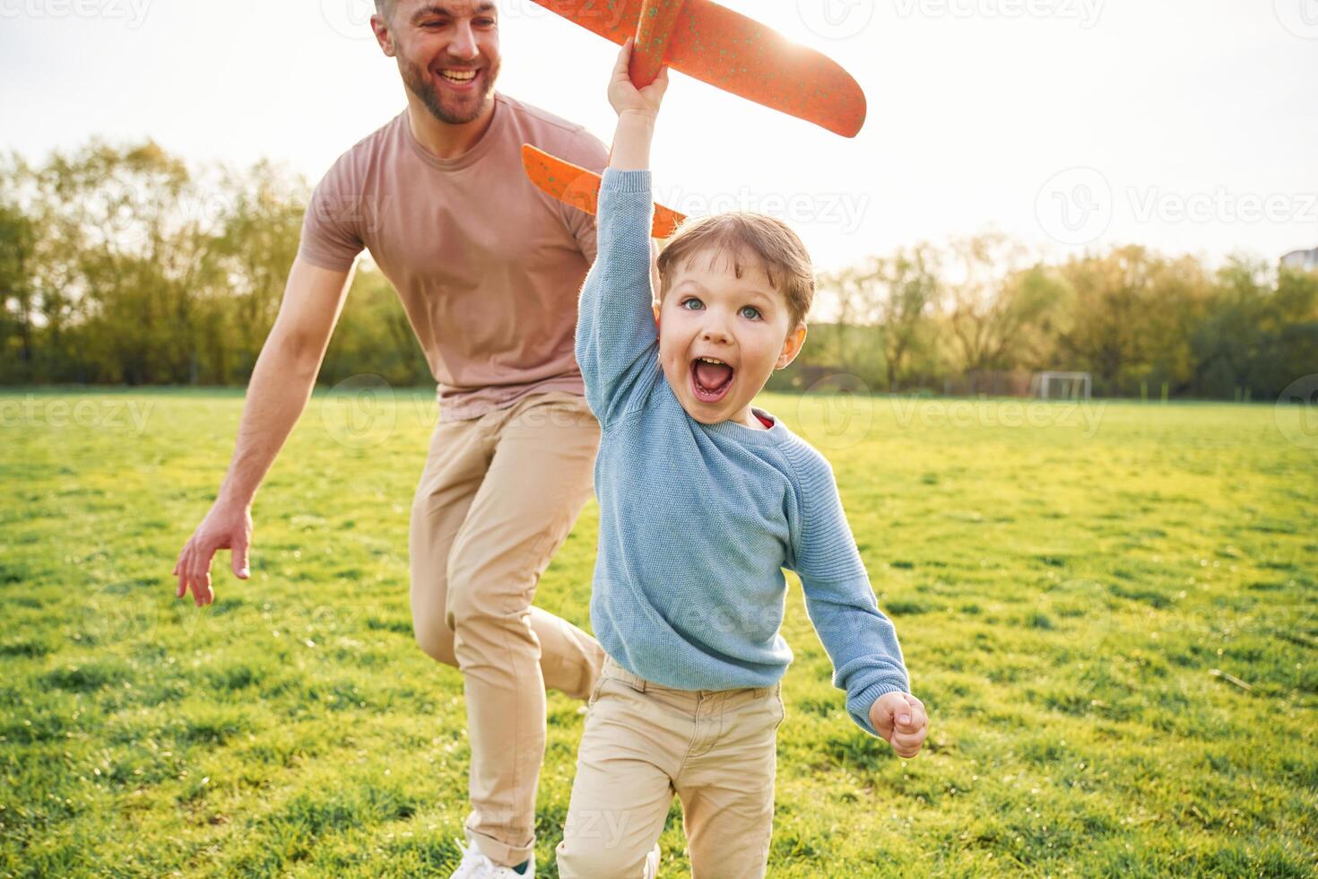 Orange, colored toy plane, playing. Happy father with son are having fun on the field at summertime photo