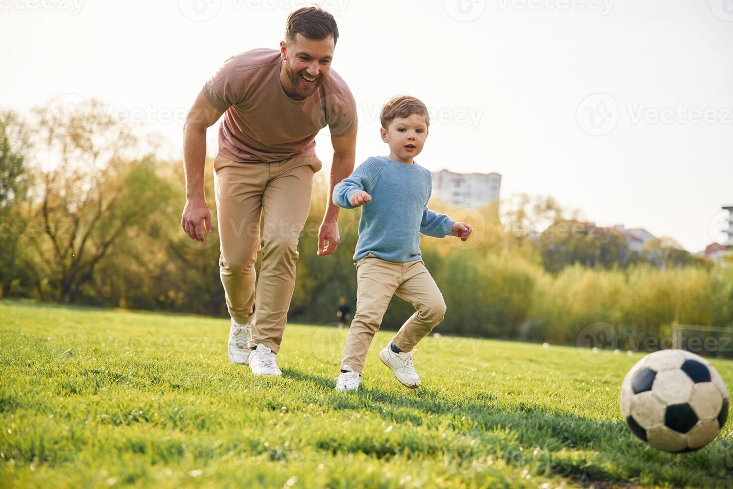 Game, of soccer. With ball. Happy father with son are having fun on the field at summertime photo