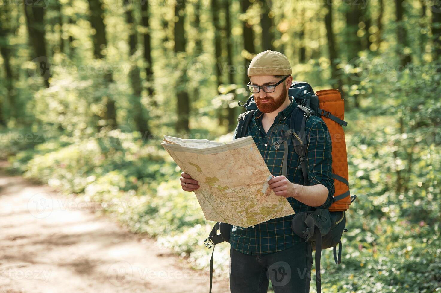 Old ,,fashioned paper map in hands. Bearded man is in the forest at daytime photo