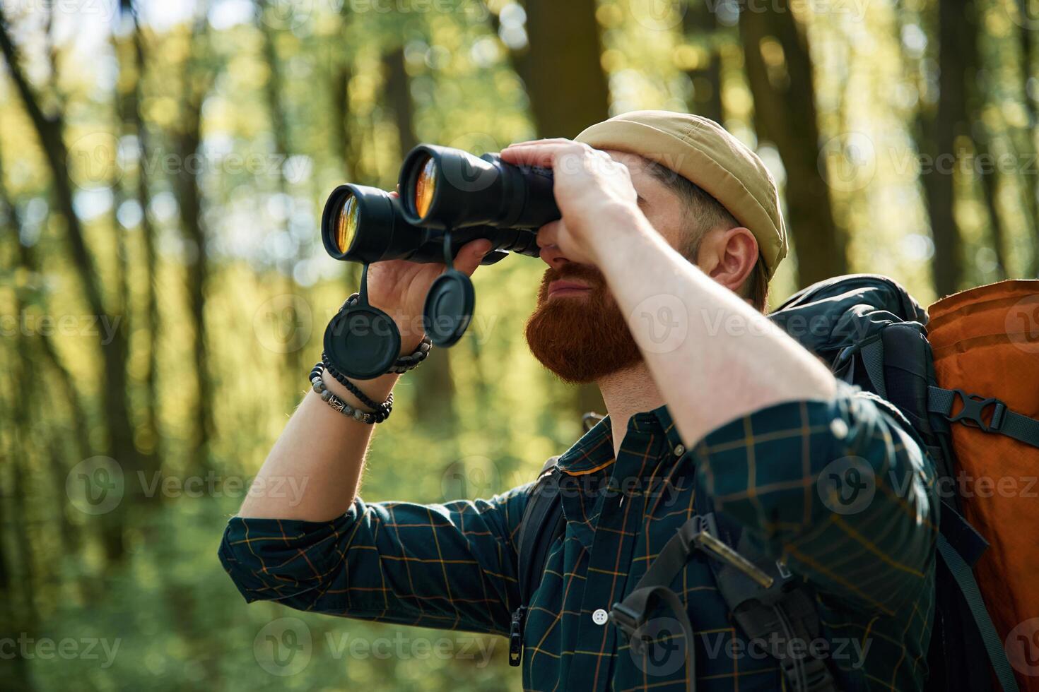 Using binoculars. Bearded,, man ,is in the forest at daytime photo