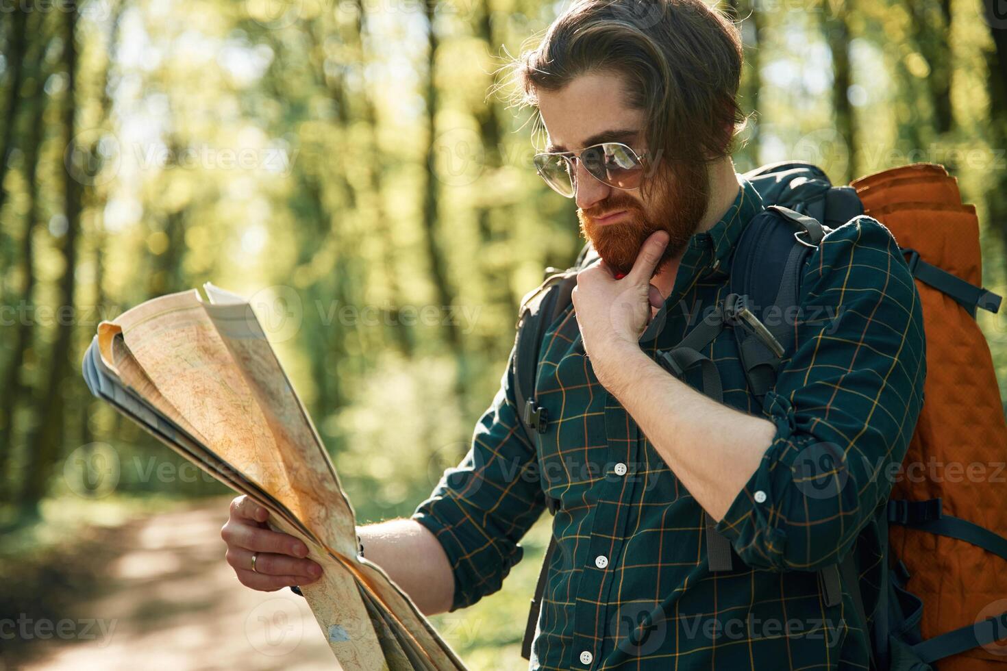 Old fashioned, paper, map in hands. Bearded man is in the forest at daytime photo