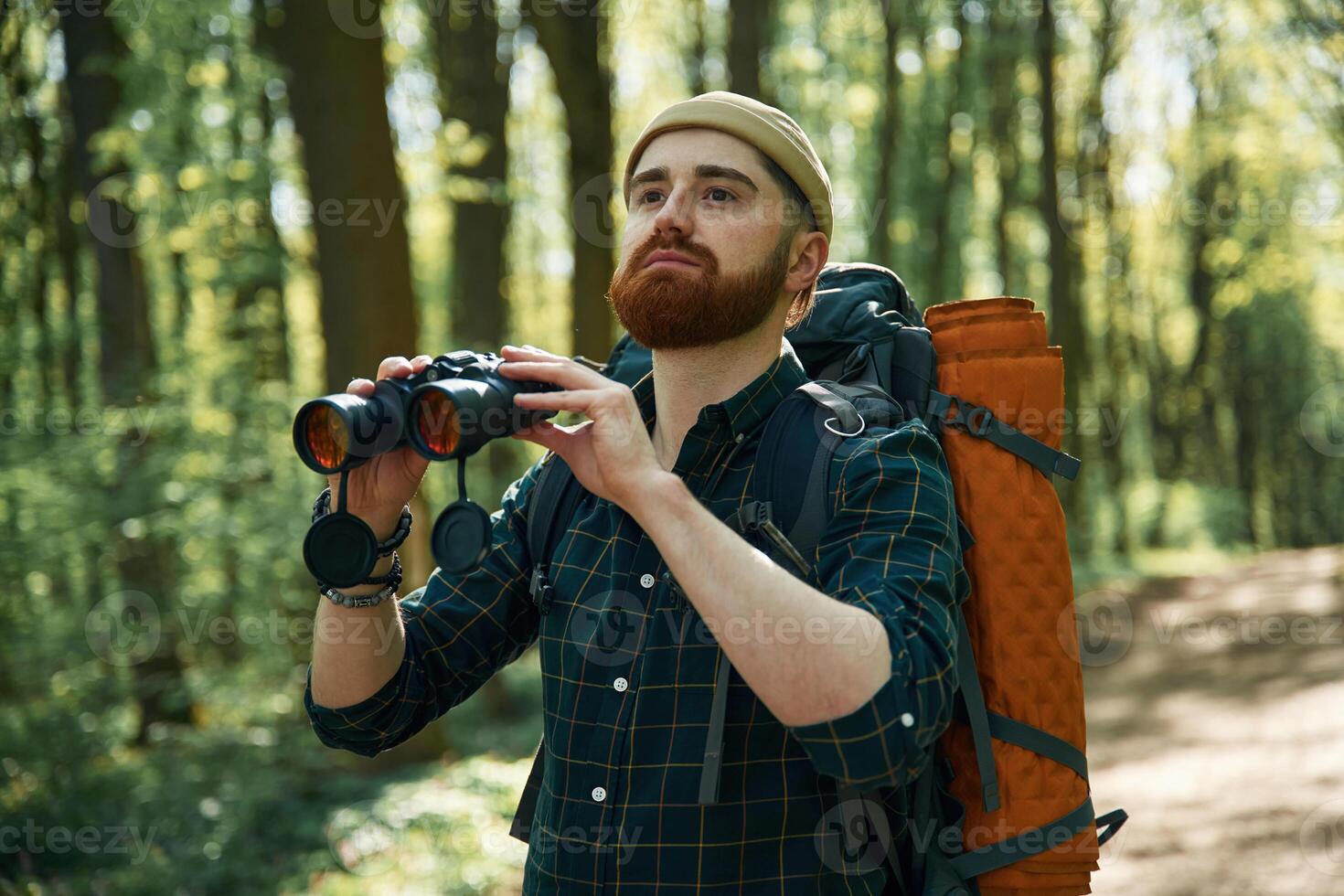 Using ,binoculars. Bearded man is in the forest at daytime photo
