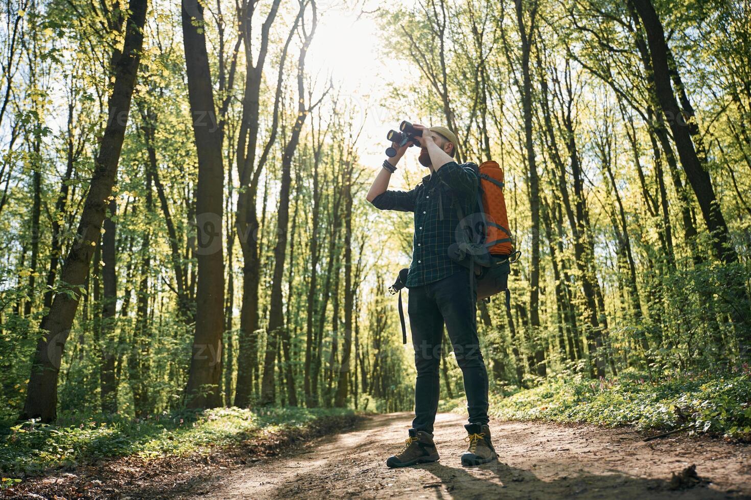 Looking far away by using binoculars. Bearded man is in the forest at daytime photo
