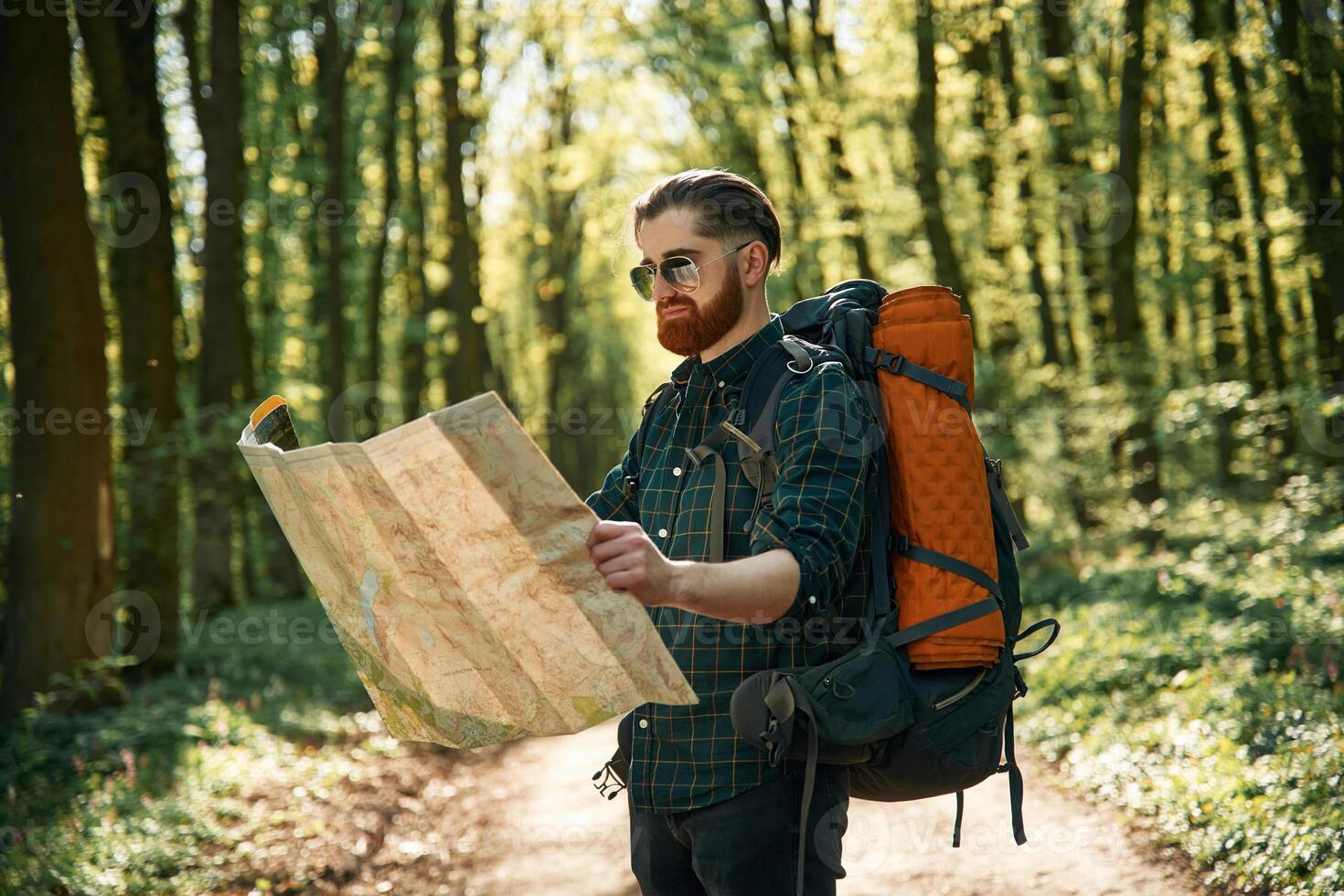 Old fashioned ,pape,r map in hands. Bearded man is in the forest at daytime photo