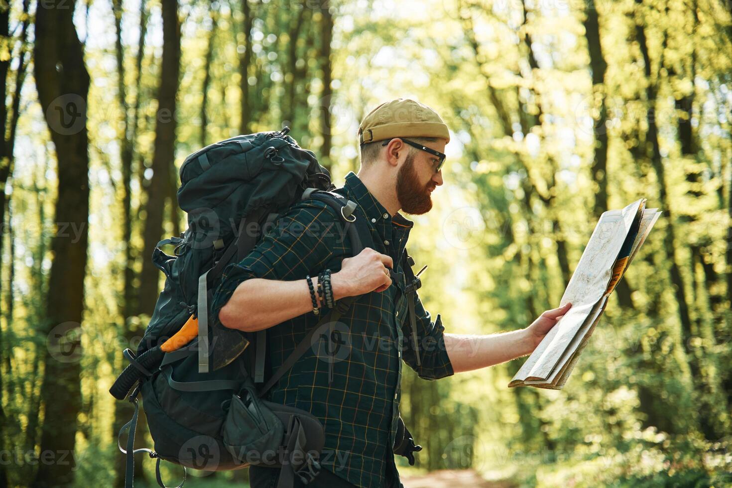 Big paper map. Bearded man, is in the forest at daytime photo