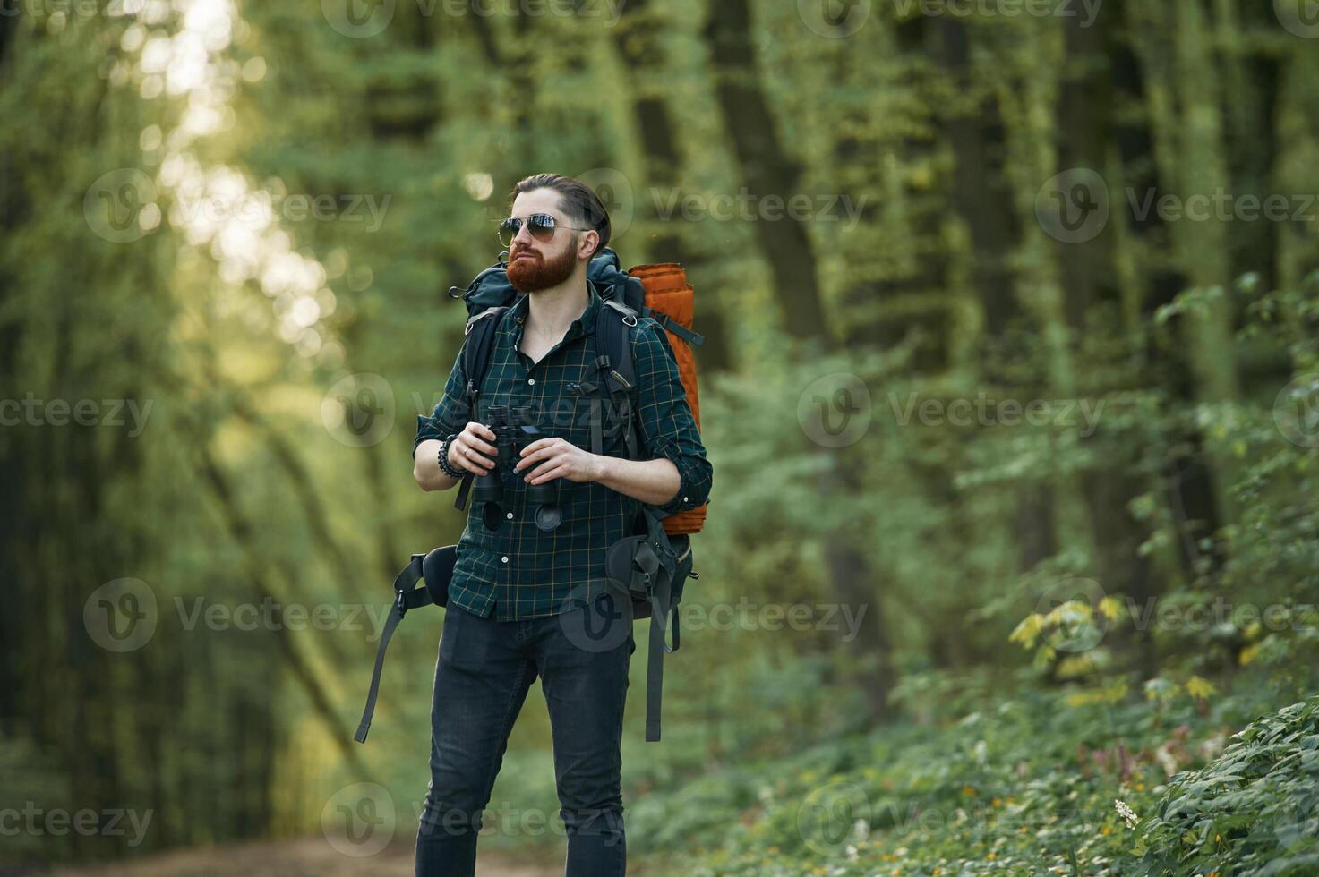 On the ,pathway with binoculars. Bearded man is in the forest at daytime photo