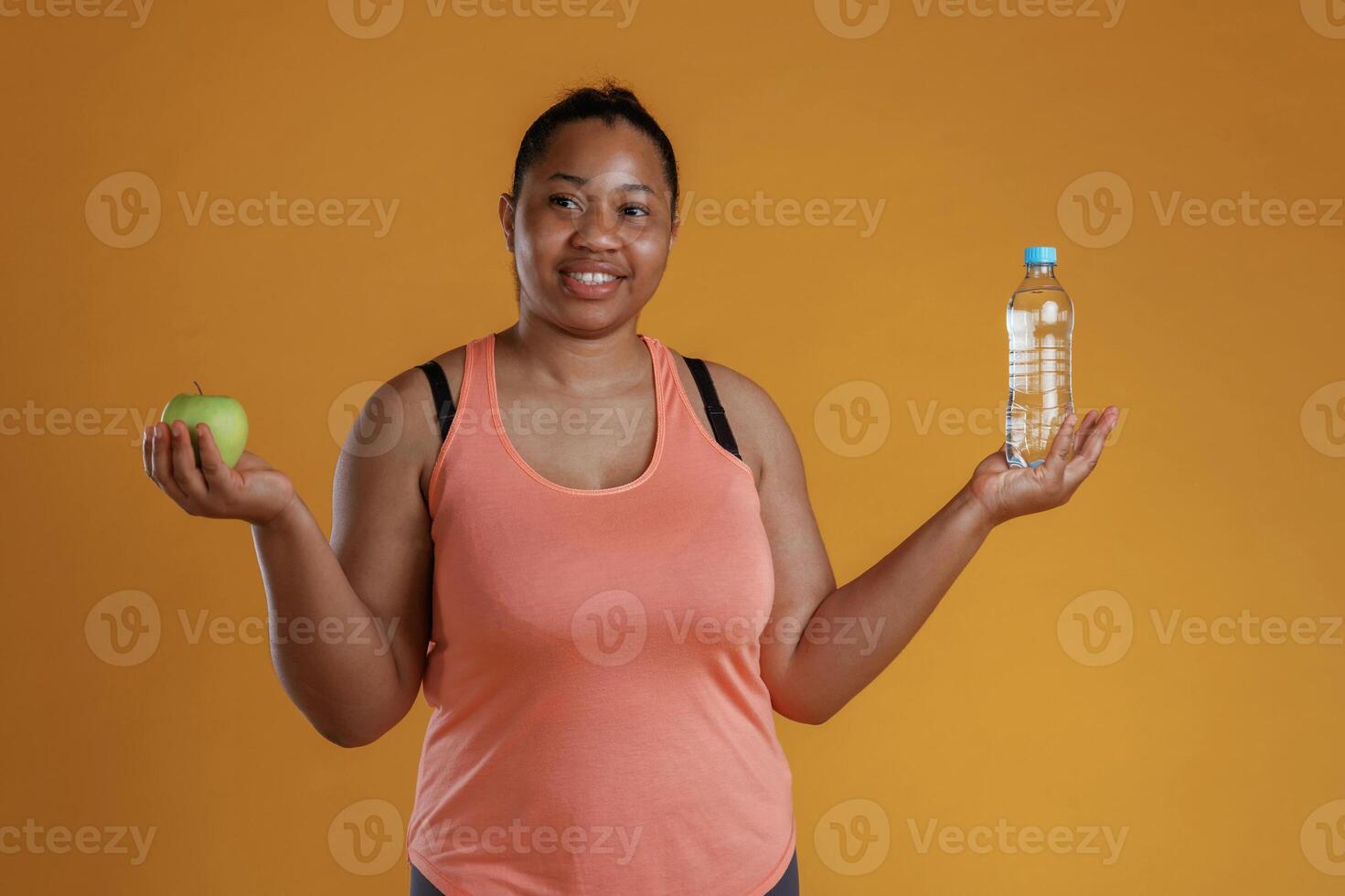 Green apple and bottle ,of water in hands.... African American woman is in the studio against yellow background photo