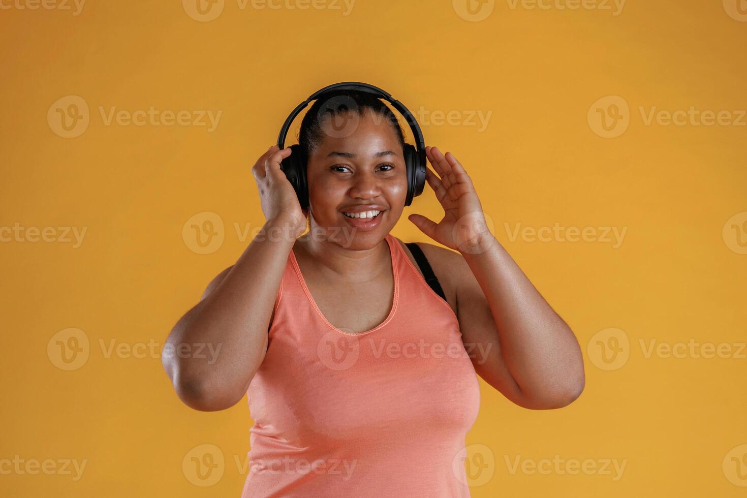 Front view, in headphones, listening to music. African American woman is in the studio against yellow background photo