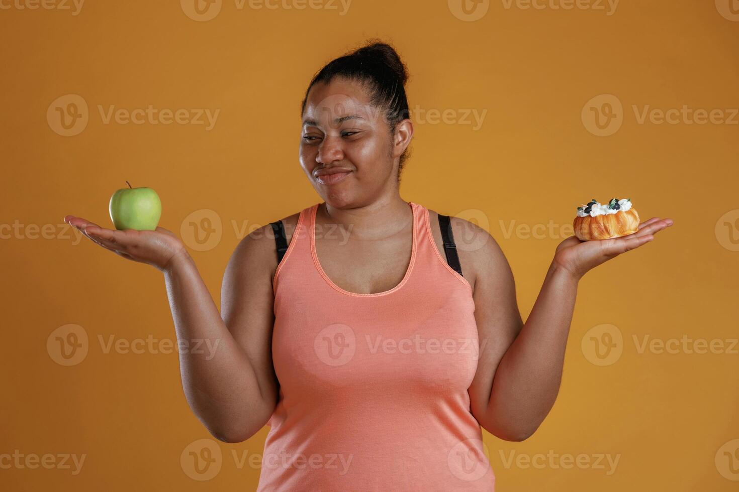 Apple or cake. Diet conception. African American woman is in the studio against yellow background photo