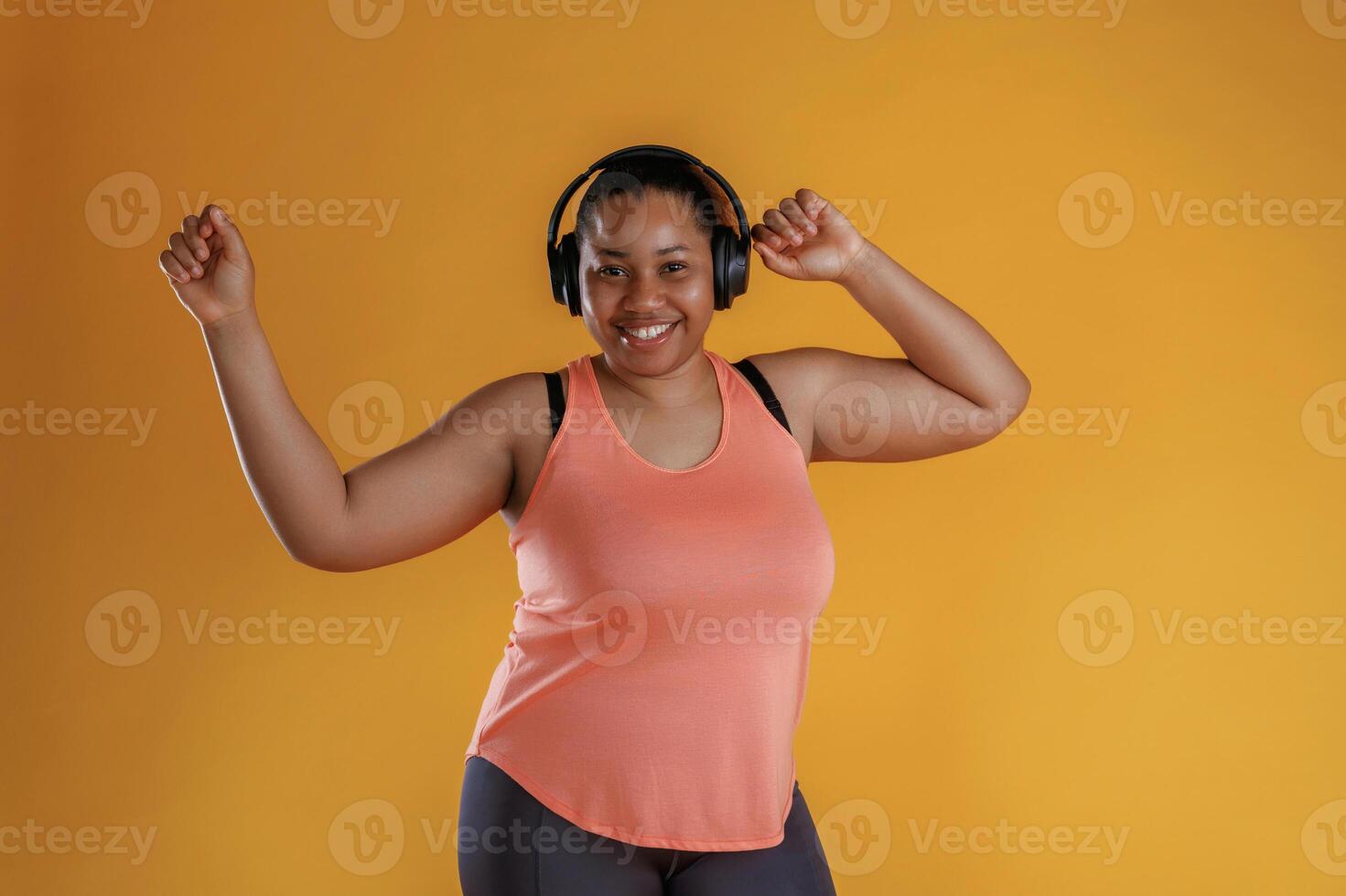 Front view, in ,headphones, listening to music. African American woman is in the studio against yellow background photo
