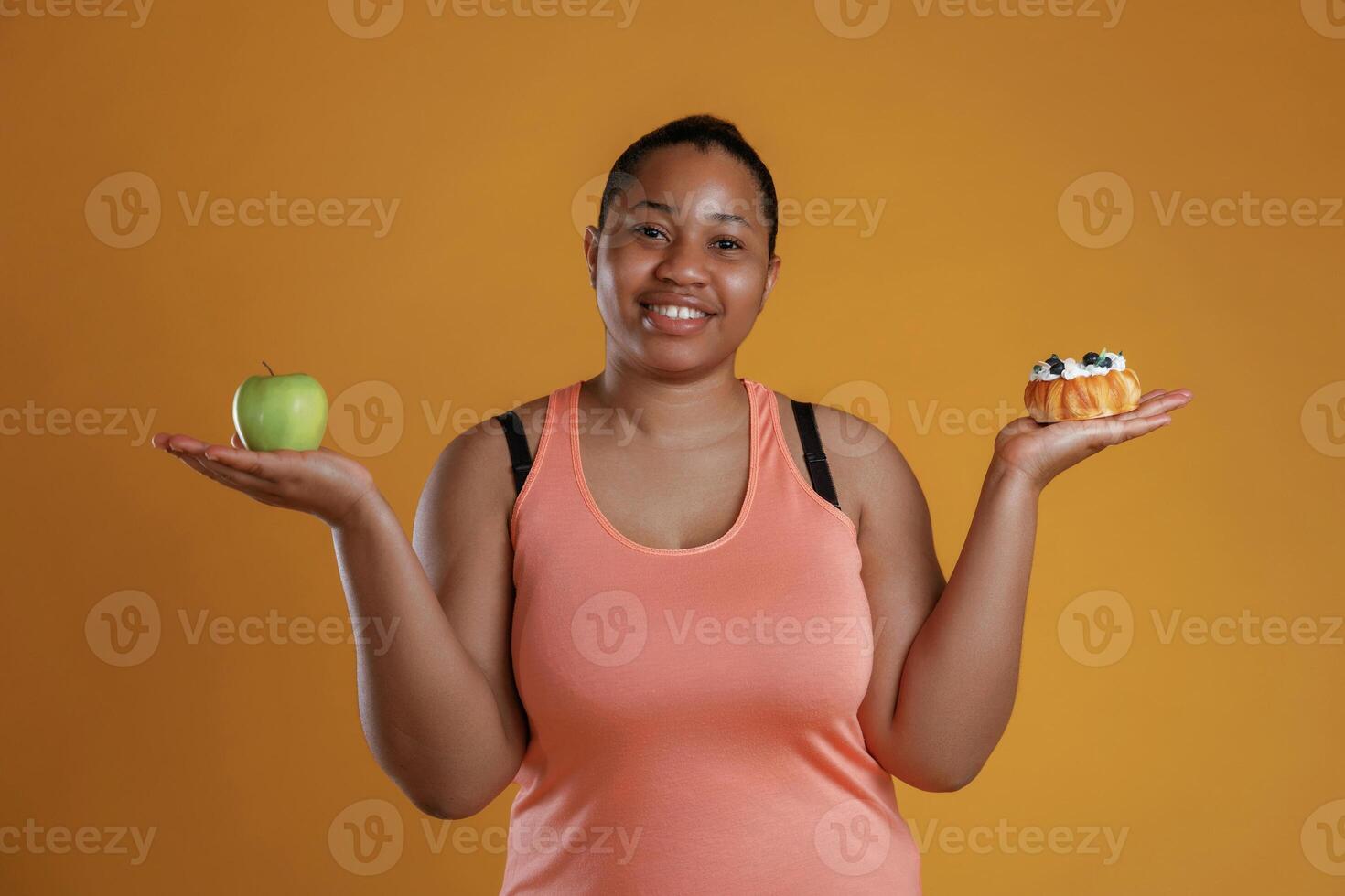 Apple or cake.. Diet conception. African American woman is in the studio against yellow background photo