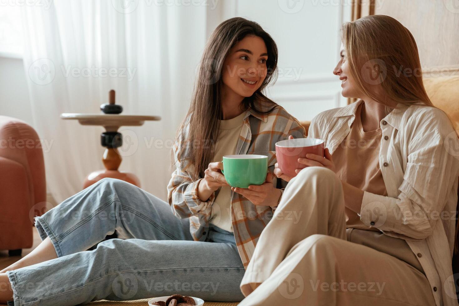 Conversation, with cups ,of ,,drink. Two happy young female best friends are indoors photo