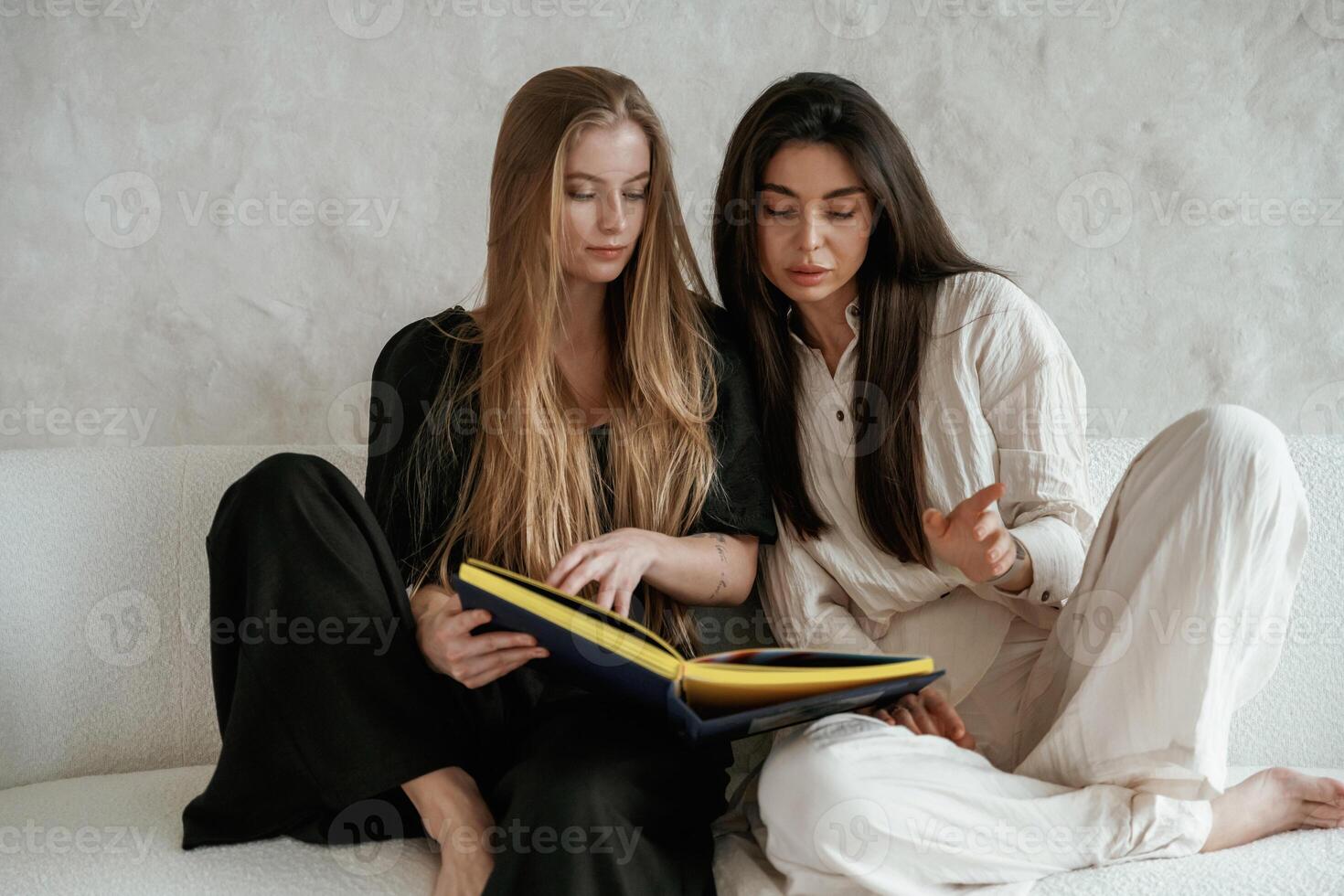 Holding ,and looking at album with photos. Two happy young female best friends are indoors photo