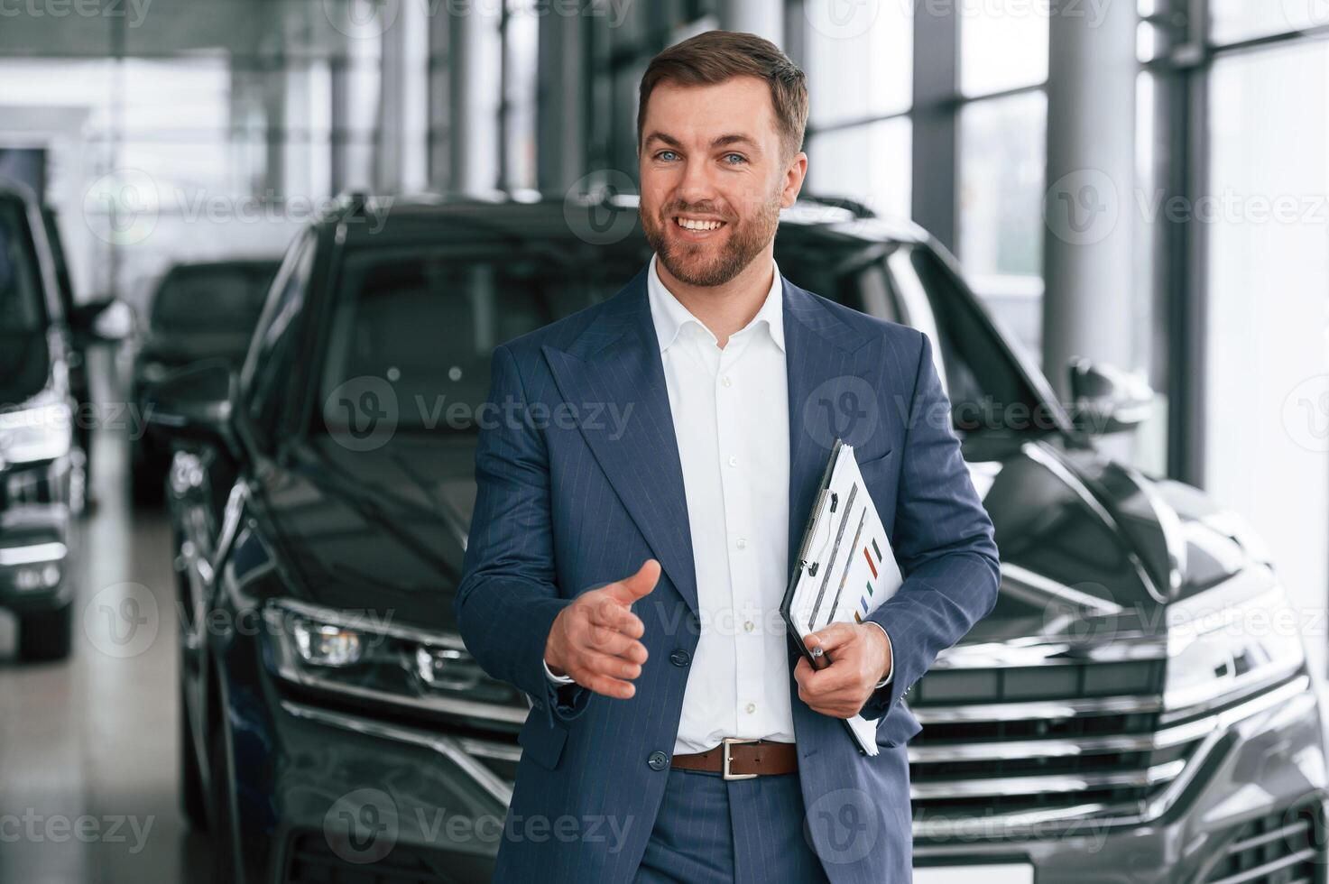 Making a deal, giving ,,a hand, holding notepad. A businessman is in a car dealership photo