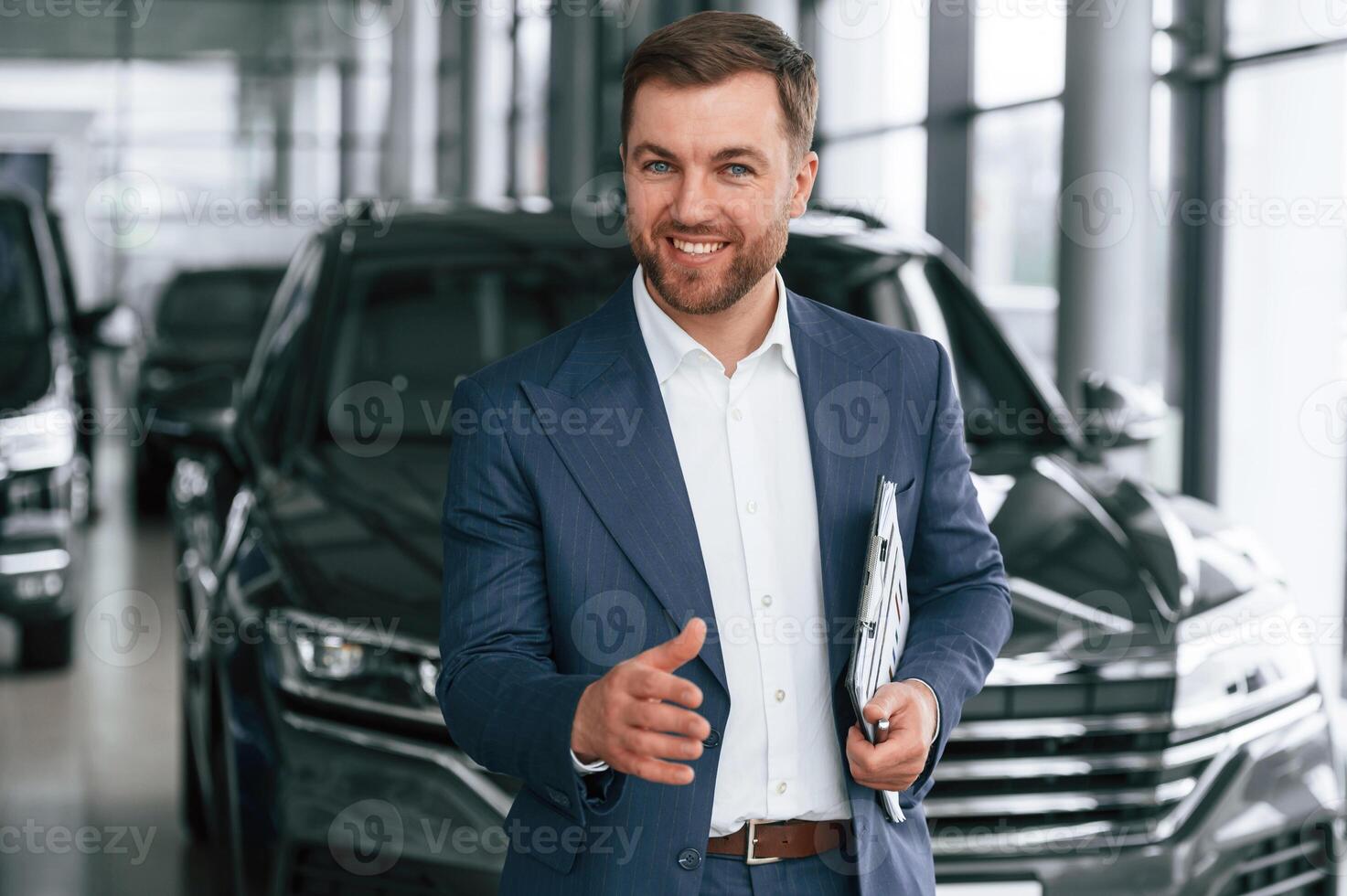 Making ,a deal, giving a hand, holding notepad. A businessman is in a car dealership photo