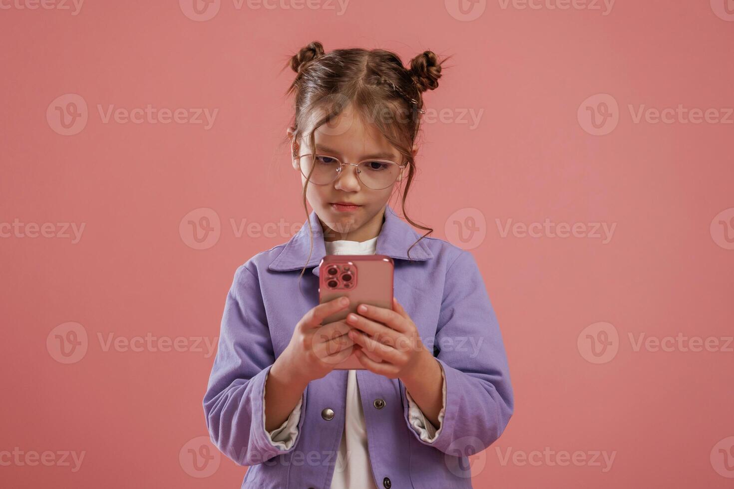 Focused by using smartphone., Cute little girl is against pink background photo