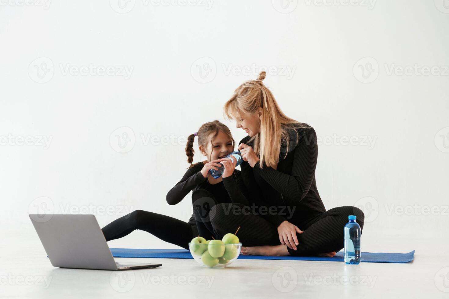 Silver colored laptop, apples and water... Mother and little daughter are in fitness clothes on yoga mat photo