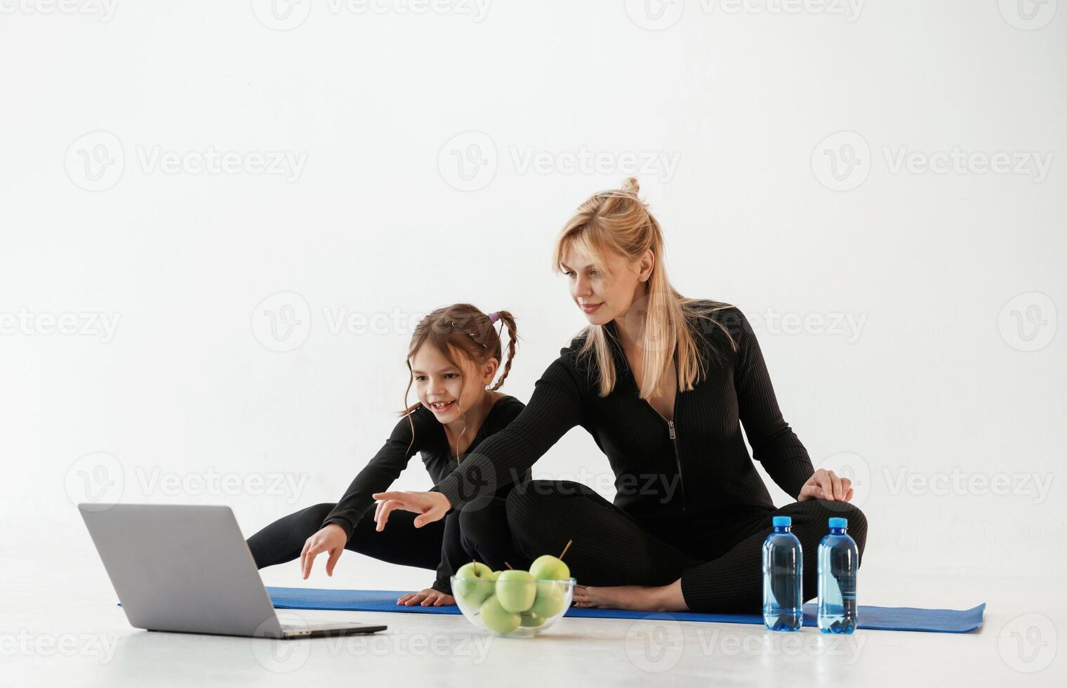 Silver colored, laptop, apples, and, water. Mother and little daughter are in fitness clothes on yoga mat photo