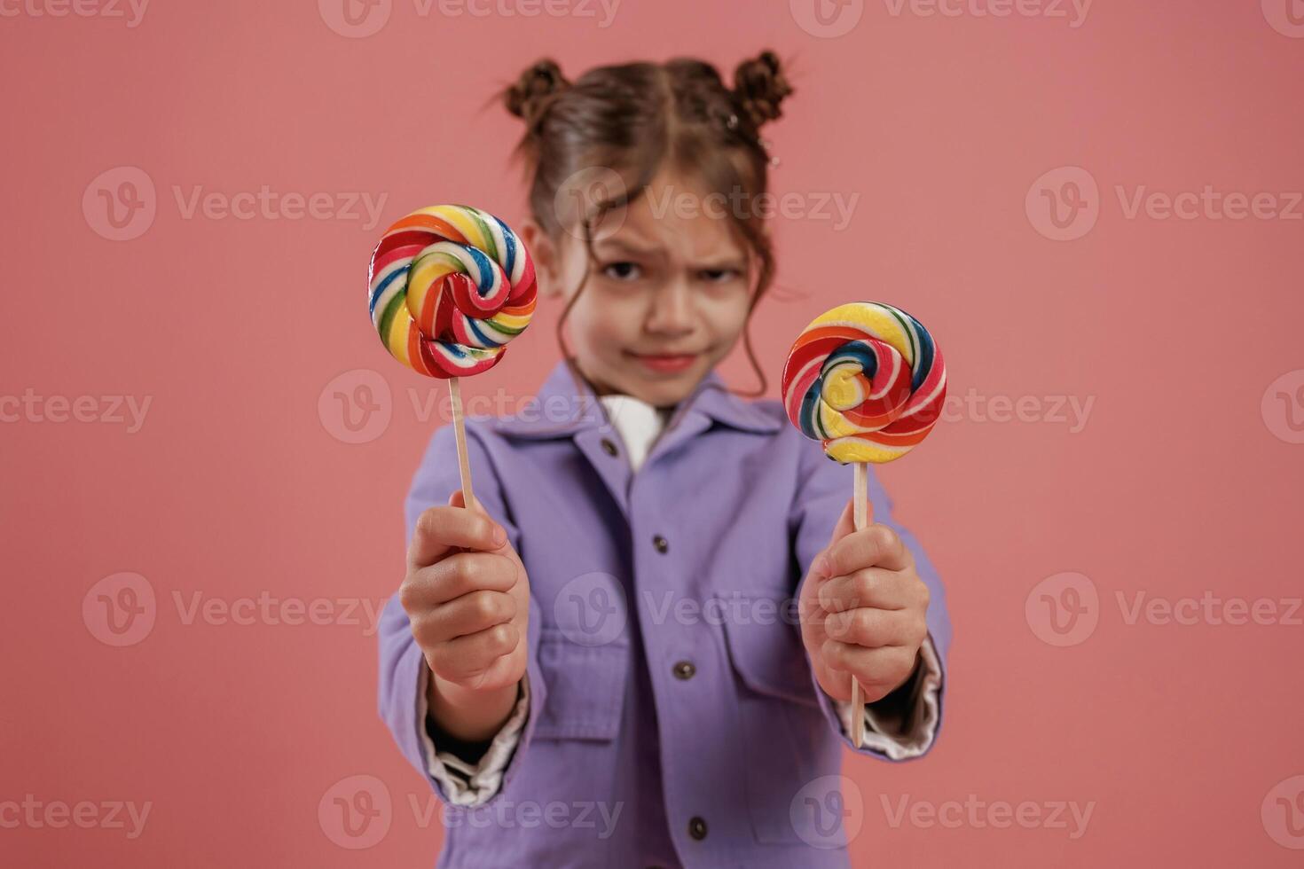 Posing and showing two candies. Cute little girl is against pink ,,background photo