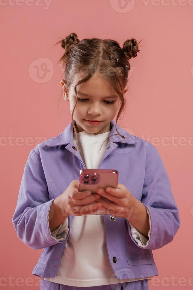 Focused by using, smartphone,, Cute little girl is against pink background photo