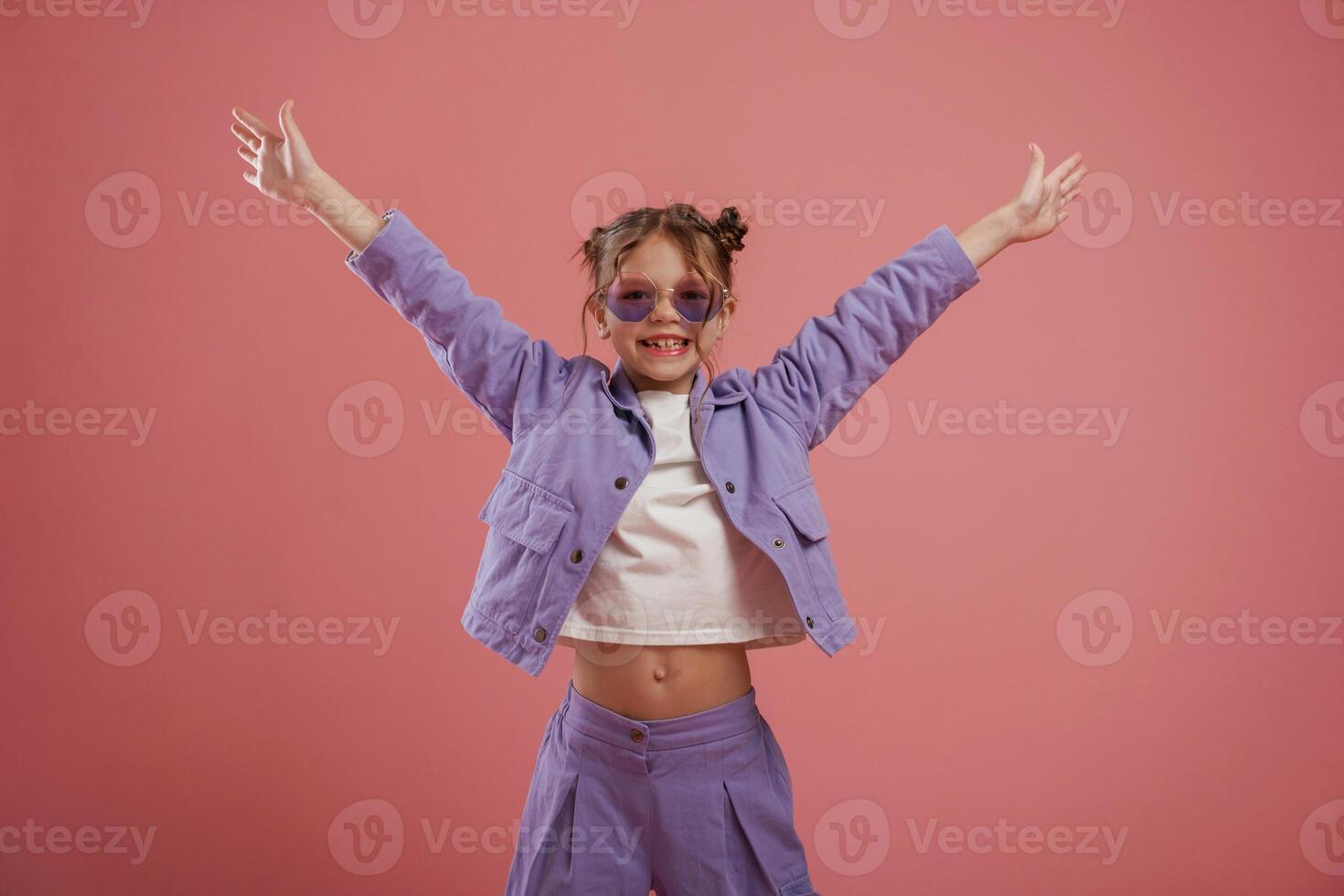 Smiling, with hands up and on the sides. Cute little girl is against pink background photo