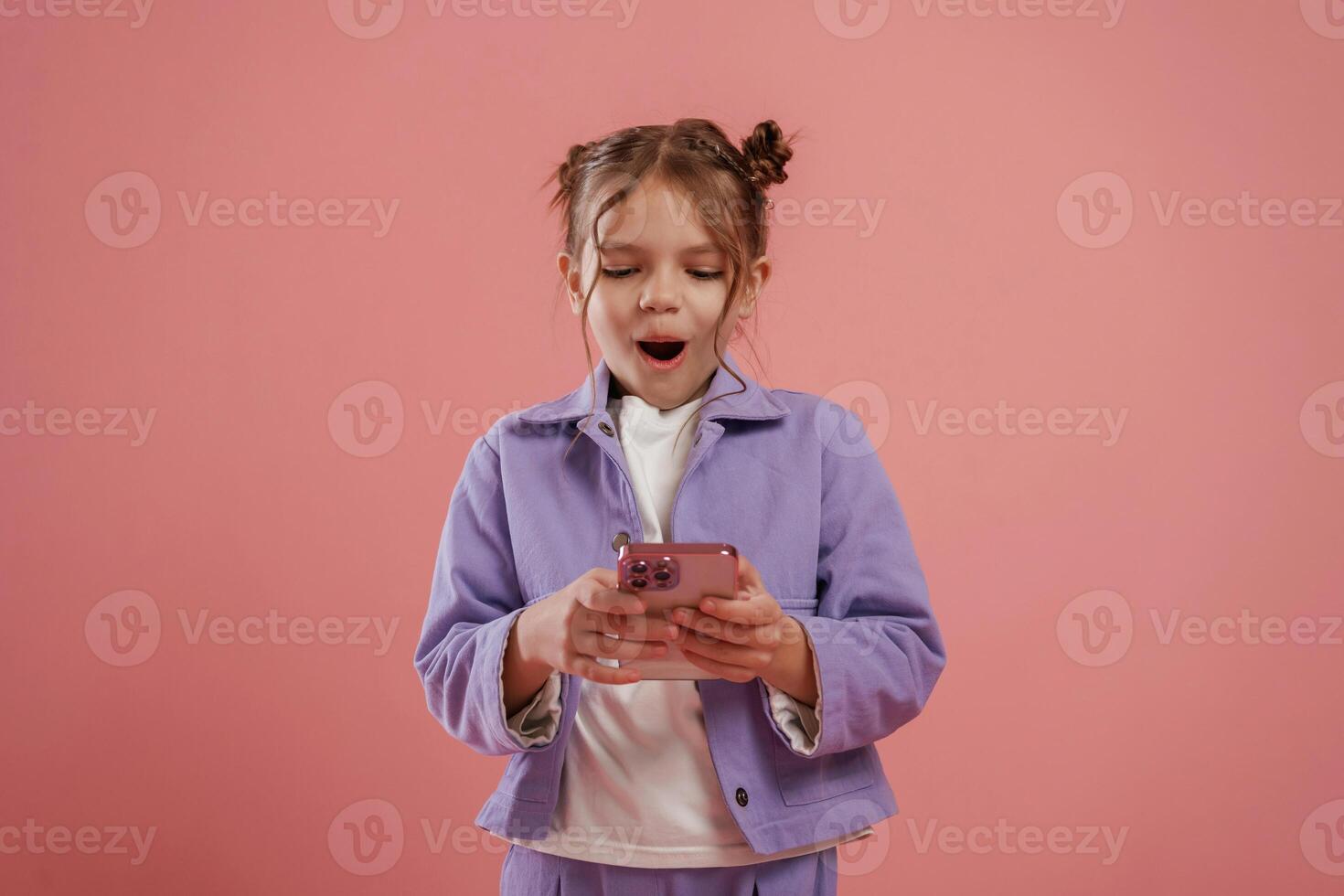 Surprised, using ,smartphone. Cute little girl is against pink background photo