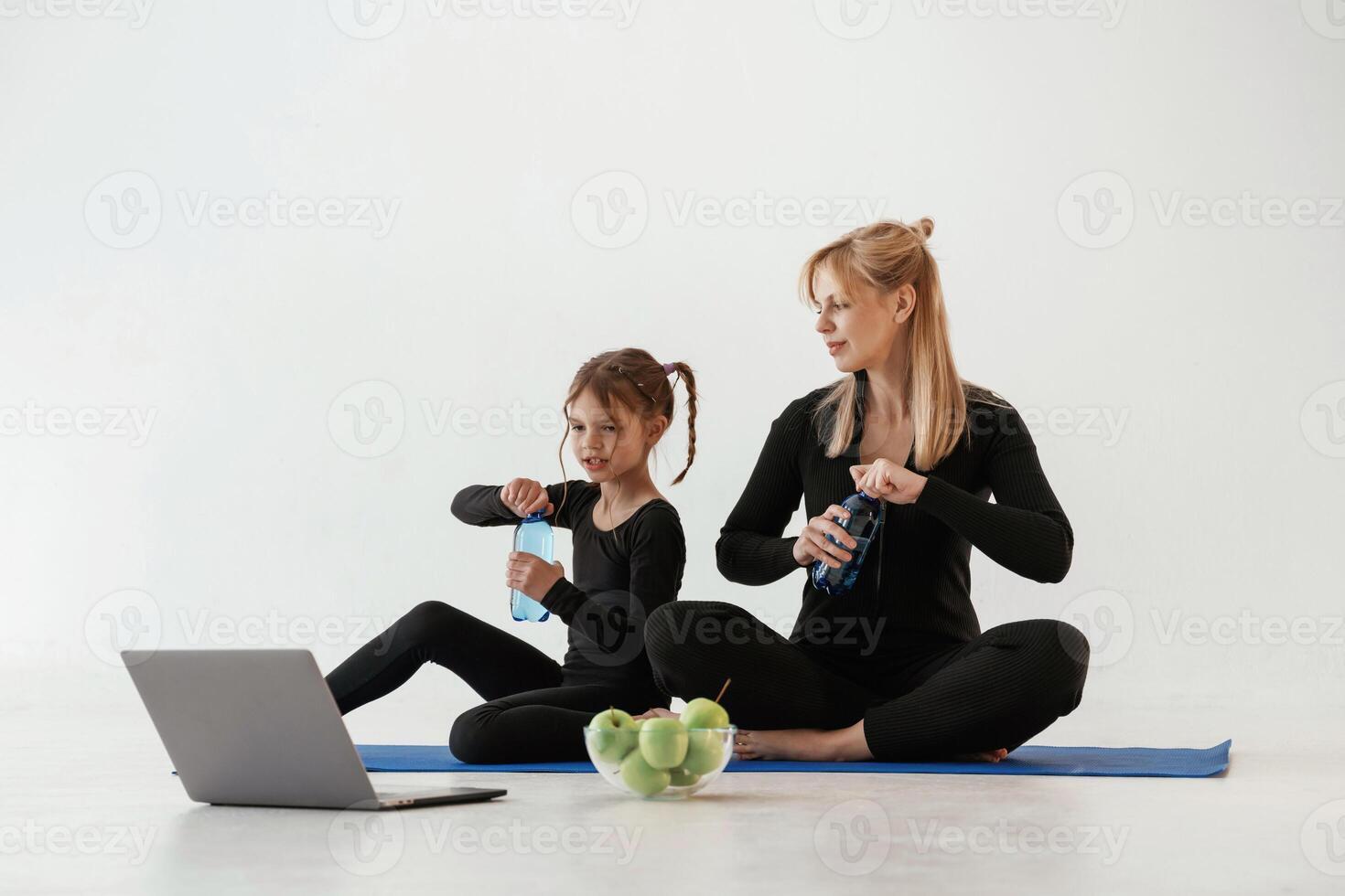 Taking a ,break, fun, laptop, water and apples. Mother and little daughter are in fitness clothes on yoga mat photo