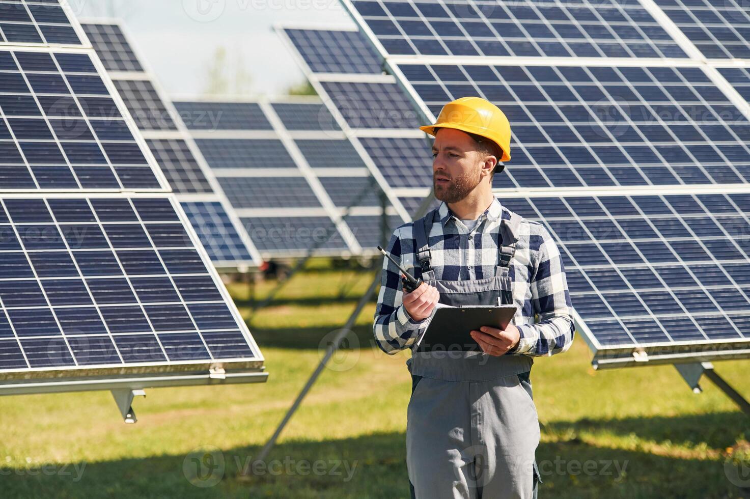 Using walkie talkie and,,, holding notepad. Engineer with photovoltaic solar panels outdoors at daytime photo