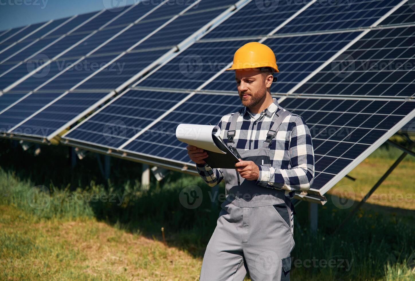 On, th,e field with notepad in hands. Engineer with photovoltaic solar panels outdoors at daytime photo