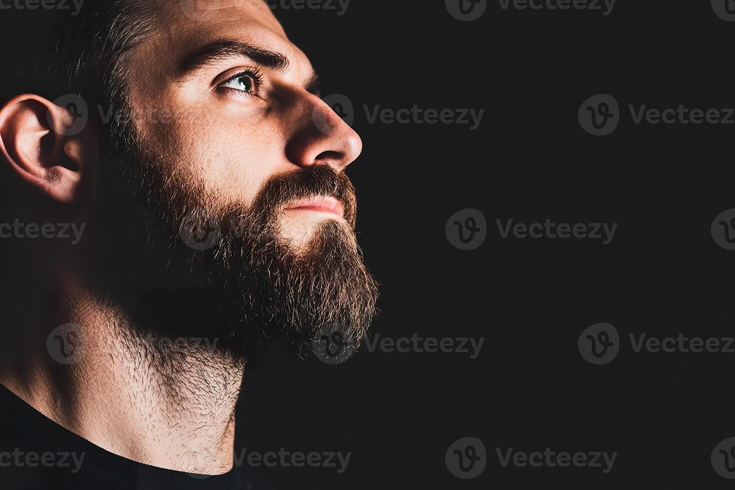 Side profile of Caucasian male with beard gazing up in dark environment Contemplative, hope, longing photo