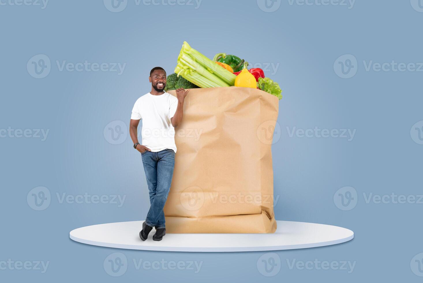 A man stands next to a large paper bag filled with fresh fruits and vegetables. He appears pleased with his grocery purchase, highlighting the convenience of modern shopping habits. photo