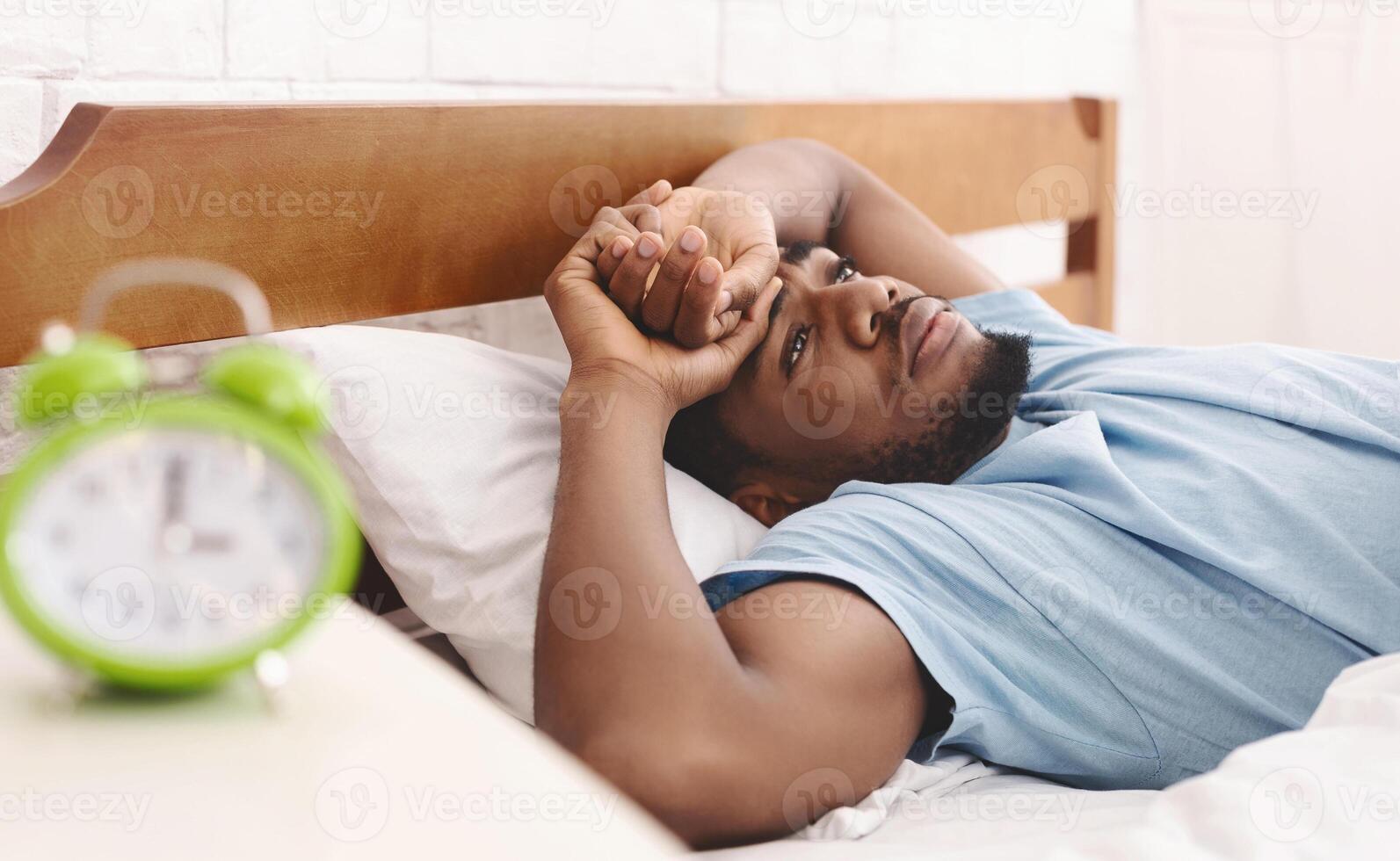 Bad mood in morning. Overslept black guy lying in bed and conteplaining, closeup photo