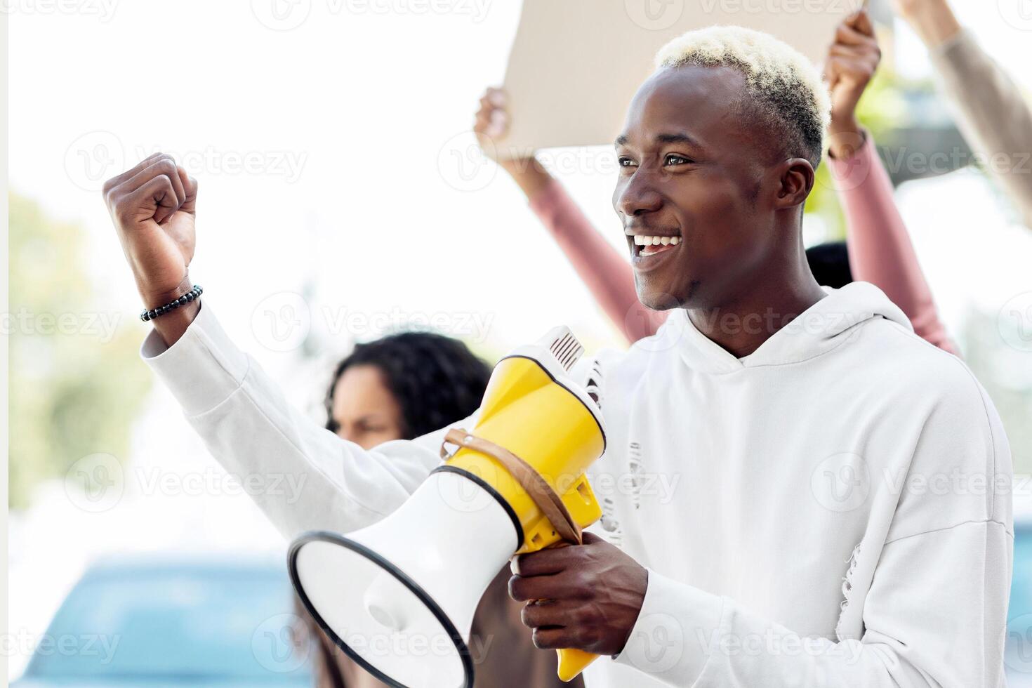Closeup of cheerful african american guy with megaphone leading students strike, chanting slogans, raising fist up, smiling and looking at copy space, side view, fight for racial equality concept photo