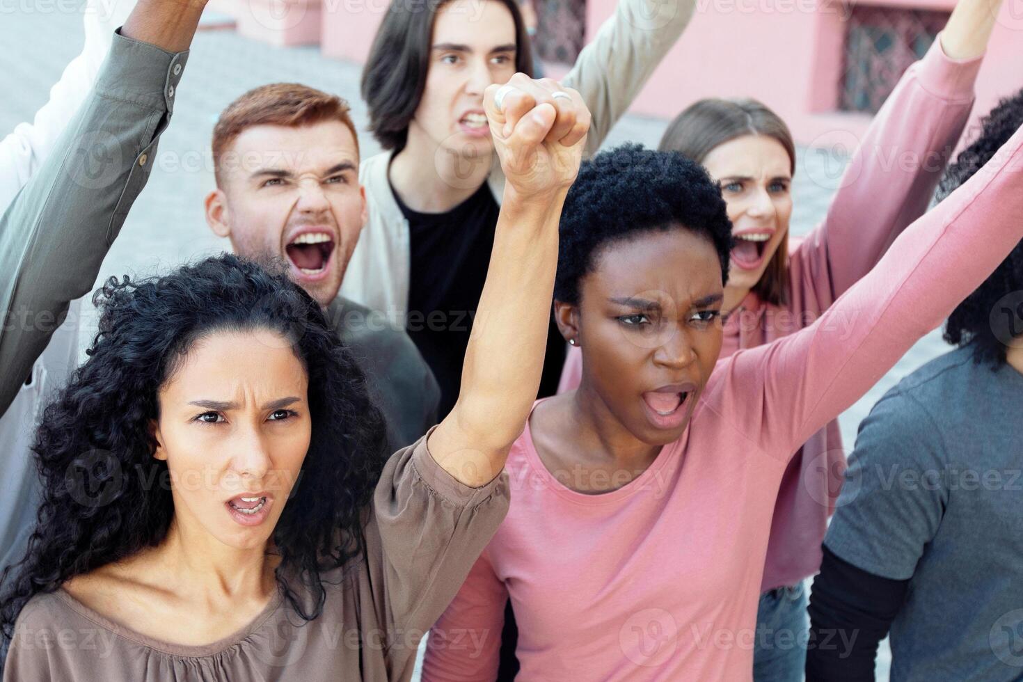 Closeup of international group of young angry men and women activists protesting against racism, descrimination, government politics outdoors, raising fists up and chanting slogans photo