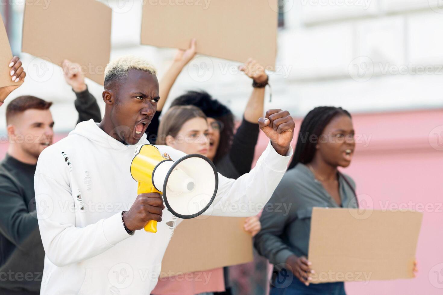 Angry black guy activist with megaphone on the street, chanting slogans and raising fist up, young african american man leading international group of demonstrators, striking against lockdown rules photo